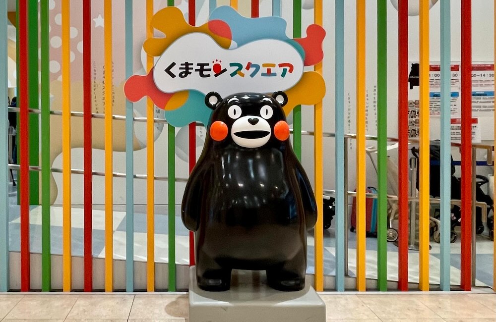 くまモンスクエアの入り口に立つくまモンの等身大フィギュア。カラフルな背景が特徴。
