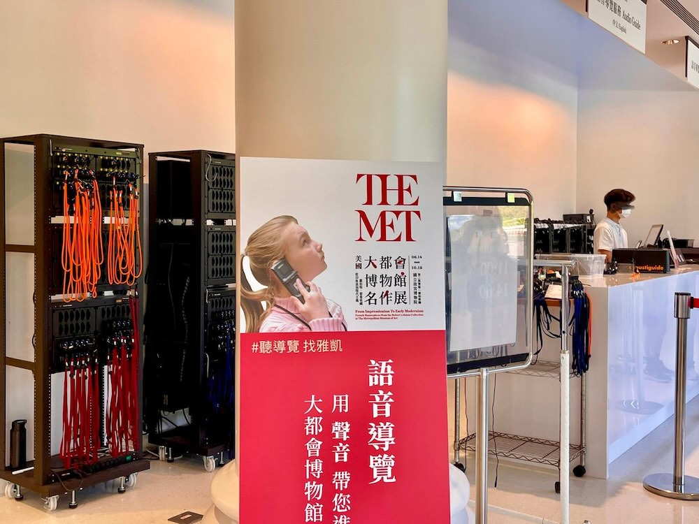 音声ガイド貸出カウンター。多言語対応のガイド機が整然と並びスタッフが対応中
