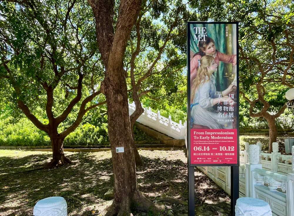 故宮博物院の木々に囲まれた庭園内に立つ縦型バナー。ルノワール作品が印象的にプリントされている