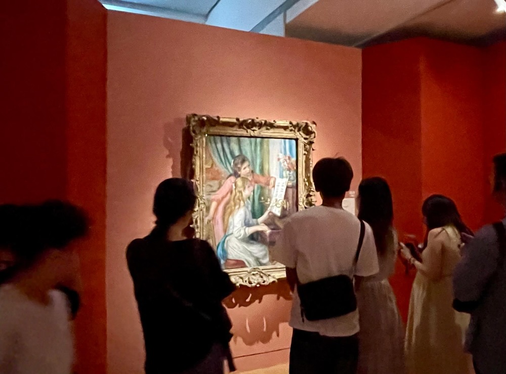 赤い壁面の展示室で、ルノワール作品を至近距離から鑑賞する来場者たち