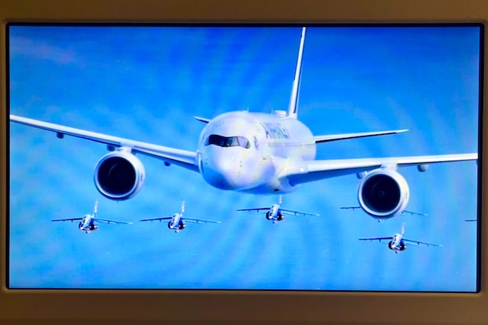 カメラに向かってバンクするA350。巨大な機体の背後に、編隊を組んだジェット機が美しいシンメトリーを成す。