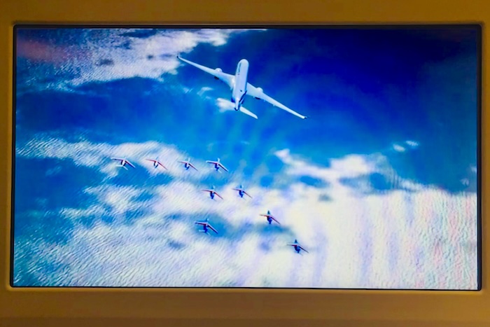 真上から捉えたショット。深い青の海と白い雲の間を、銀色の翼と色鮮やかなスモークが切り裂いていく。