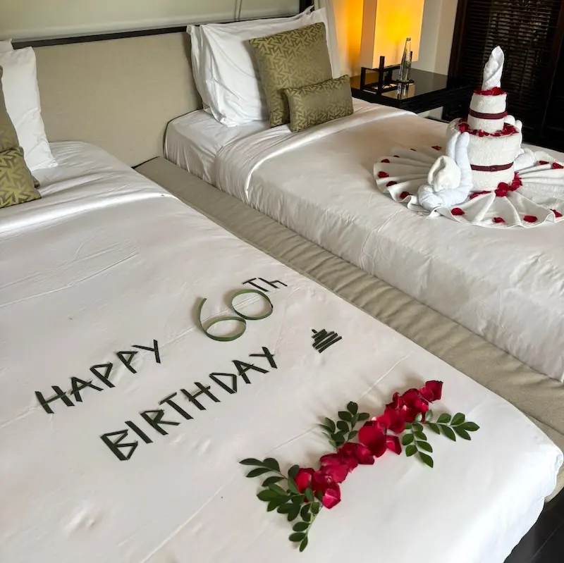 ツインベッドにHAPPY 60th BIRTHDAYの文字と赤い花びら、タオルアートが飾られたヴィラアイルバリの記念日デコレーション